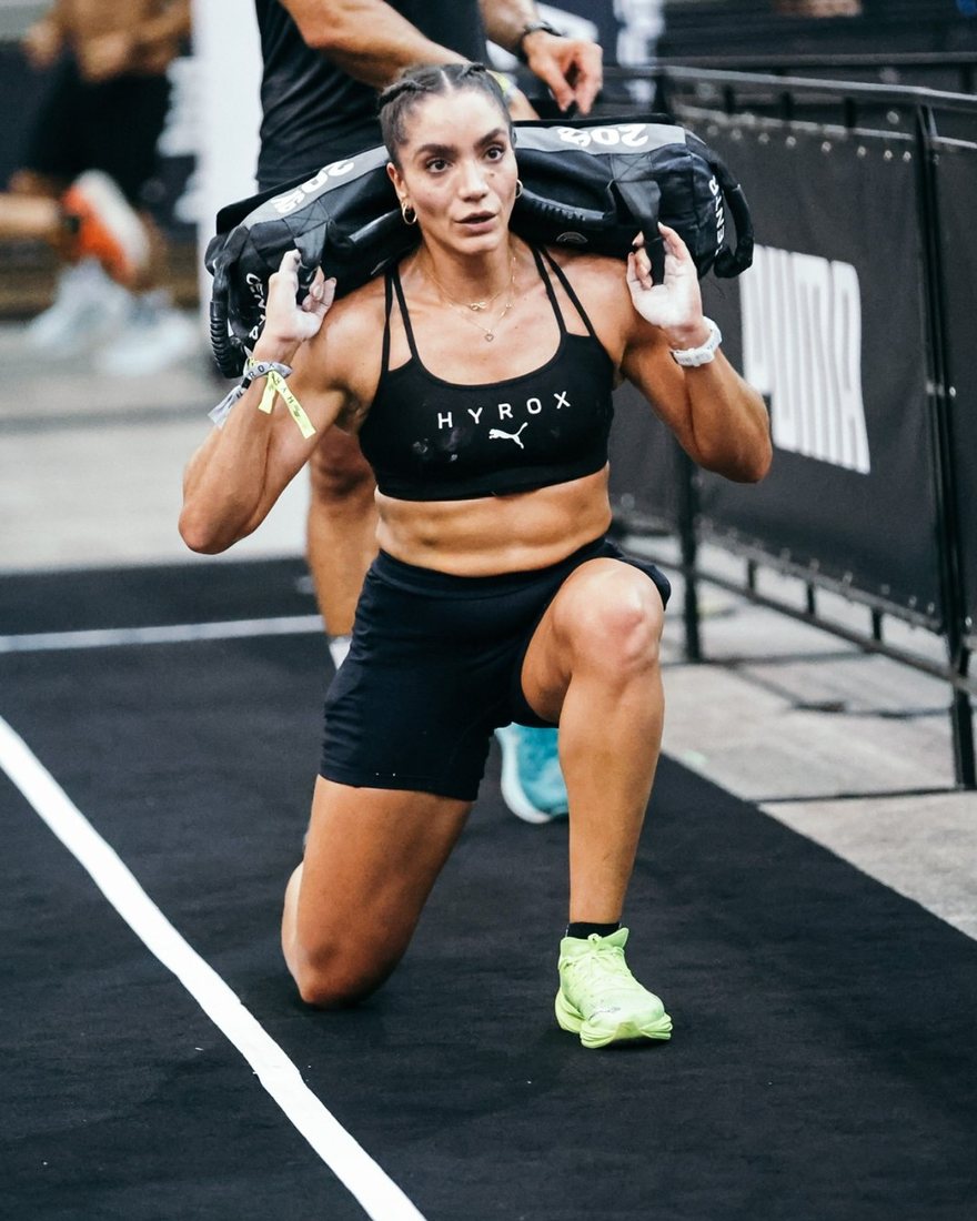 Kathy fazendo sandbag lunge numa prova de HYROX